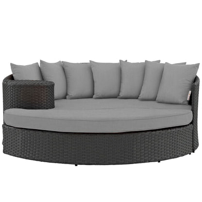 Round dark wicker outdoor daybed with light gray cushions and back pillows in a curved sectional style.