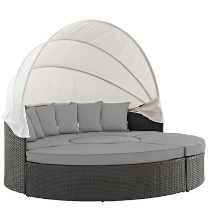 Round outdoor wicker daybed with gray cushions and a white canopy.