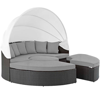 Round dark wicker outdoor daybed with white canopy and canvas gray cushions.