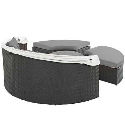 Curved dark gray wicker patio daybed with light gray cushions and white fabric drape