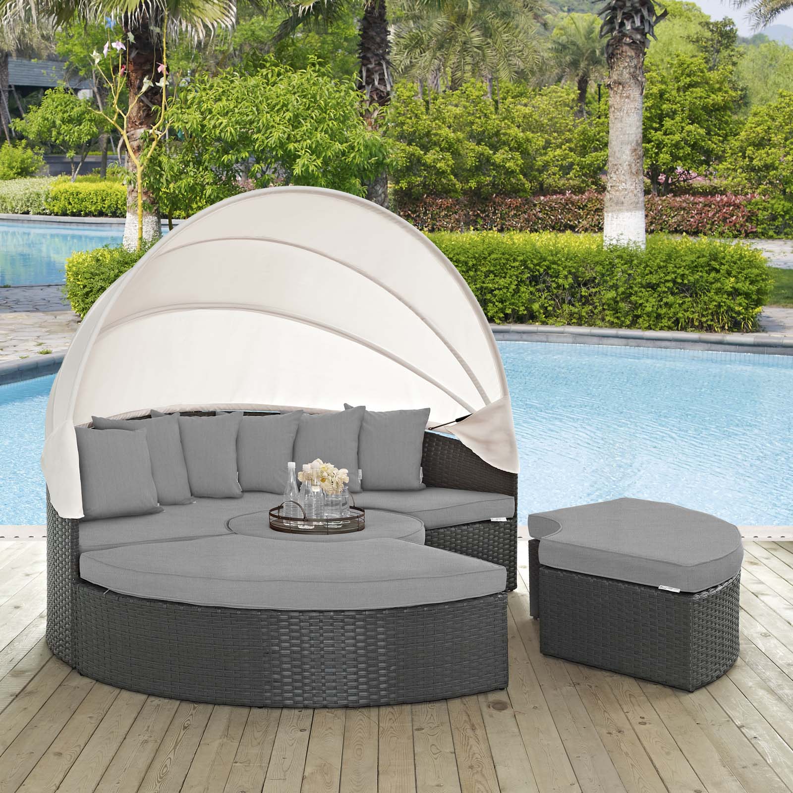 Charcoal gray round wicker outdoor daybed with a beige canopy, gray cushions & a matching ottoman by the pool.