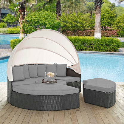 Charcoal gray round wicker outdoor daybed with a beige canopy, gray cushions & a matching ottoman by the pool.