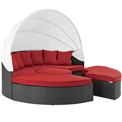 Circular dark gray wicker outdoor daybed with red cushions and a white canopy, plus a matching ottoman.
