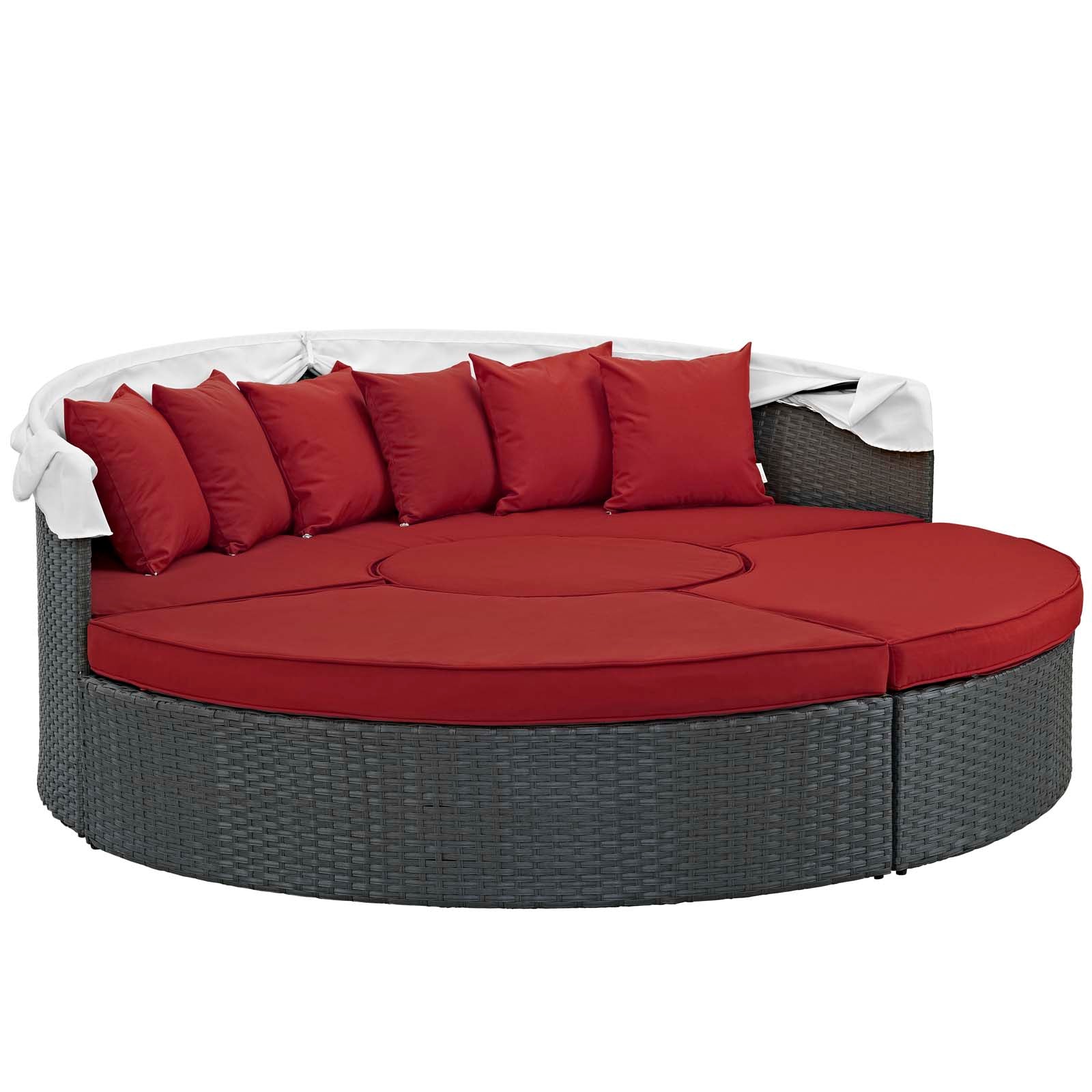 Round gray wicker outdoor daybed with red cushions and pillows, white throw blanket draped over the back.