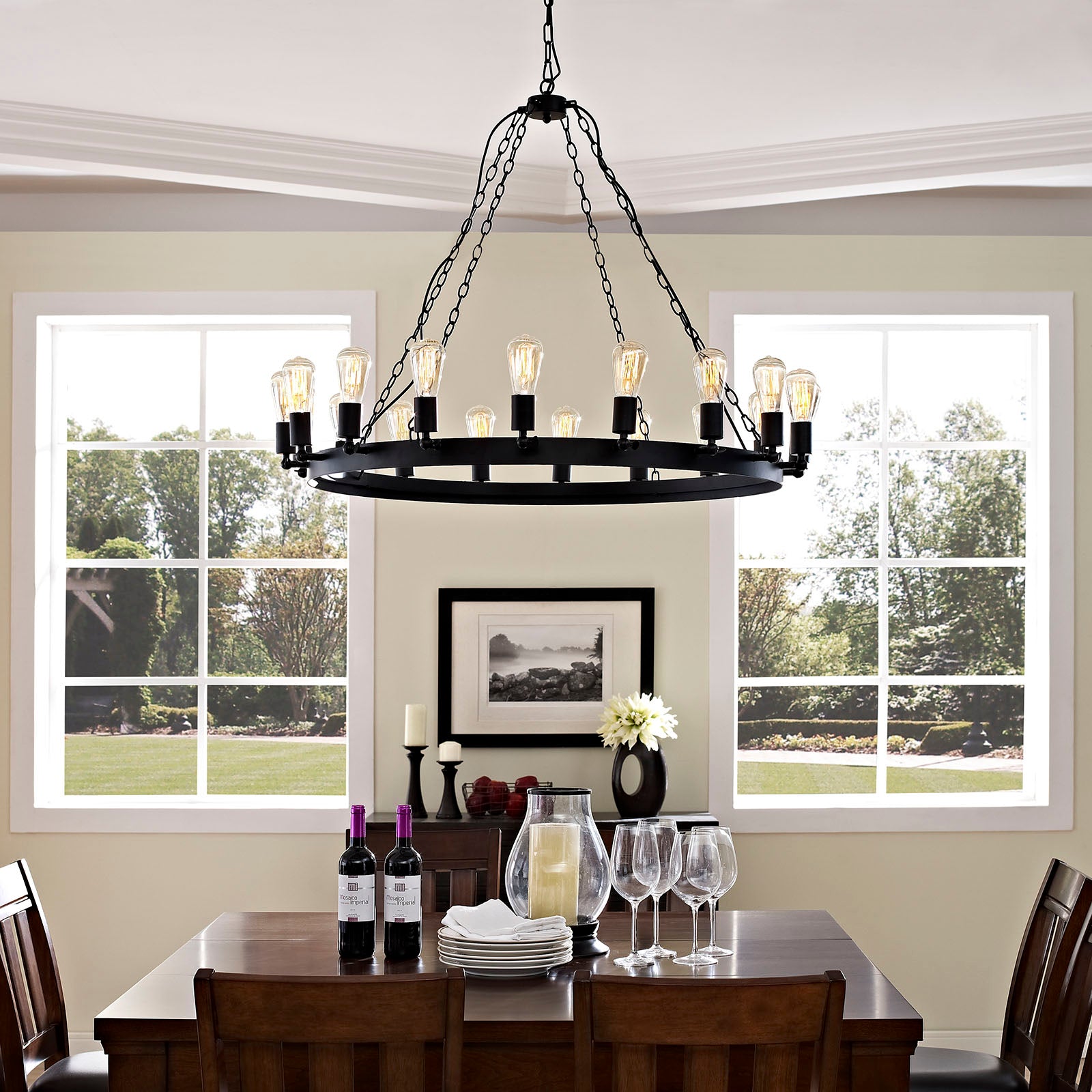 Black circular iron chandelier with candle bulbs over a brown wooden dining table in a sunlit farmhouse dining room.