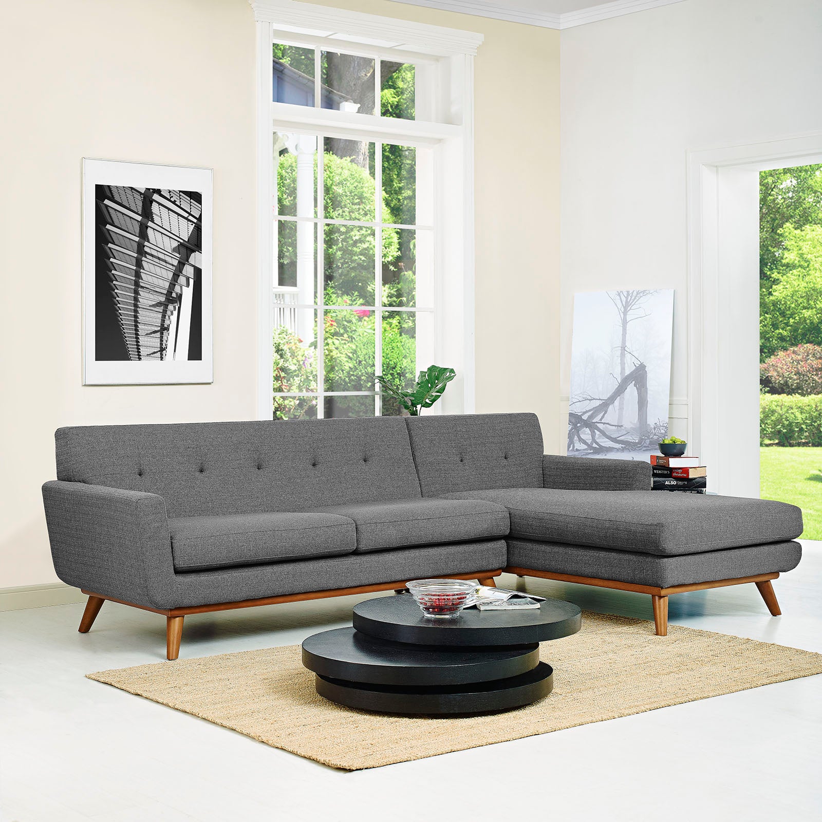 Dark gray right-facing upholstered fabric sectional sofa with chaise, wooden legs, and a two-tier round black coffee table on a beige rug.