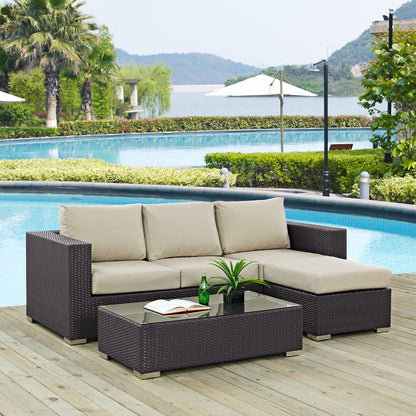 Dark brown rattan outdoor sectional with beige cushions & a glass-top coffee table on a poolside wooden deck.