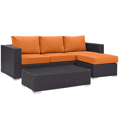 Dark brown wicker outdoor sectional with bright orange cushions, L-shaped with chaise, and matching rectangular coffee table.