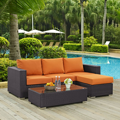 Dark brown wicker outdoor sofa set with orange cushions and a glass-top coffee table by a pool on a wooden deck.