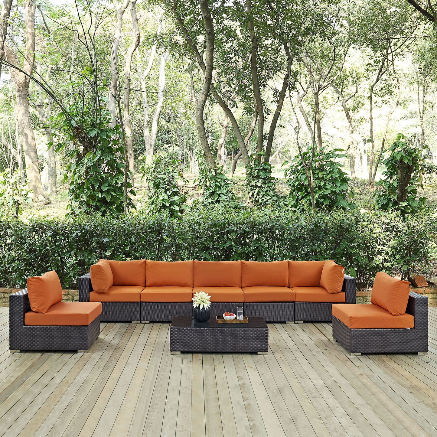 Outdoor wicker patio sectional with orange cushions on a wooden deck; includes two ottomans and a coffee table.