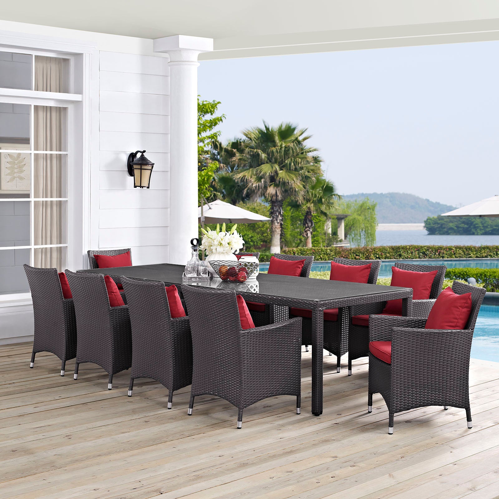 11-piece outdoor wicker dining set with red cushions, rectangular table on a wood deck by the pool