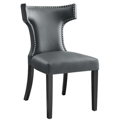 Gray faux leather dining chair with silver nailhead trim, curved wingback and dark wood legs.