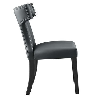 Gray vegan leather dining chair with padded backrest & nailhead trim & curved dark wood legs.