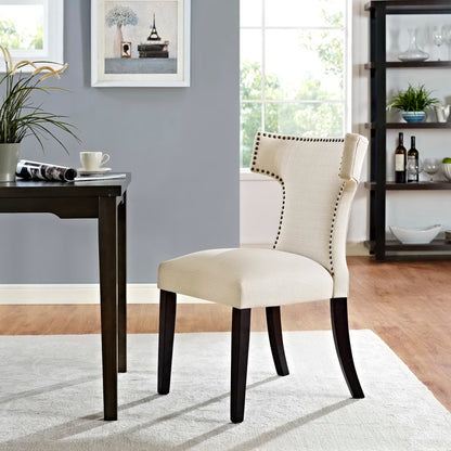 Beige fabric-upholstered dining chair with dark wood legs and nailhead trim, curved back.