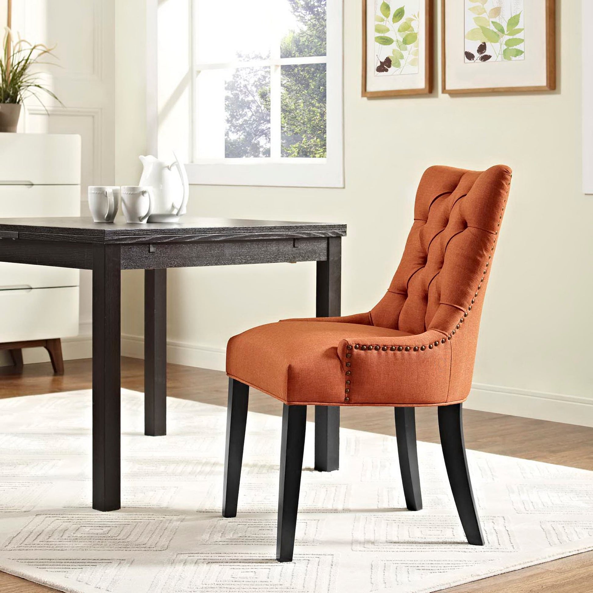 Orange tufted dining chair with nailhead trim and black legs beside a dark wood table in a bright dining room.