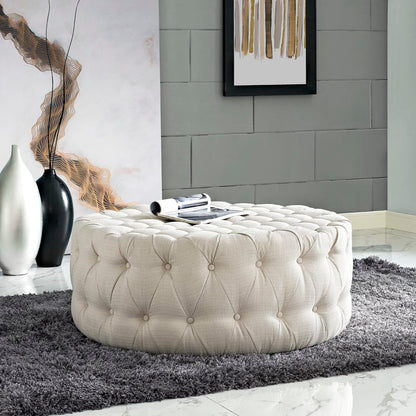Brown round tufted fabric ottoman with button detail; sits on a dark gray shag rug in a modern living room.
