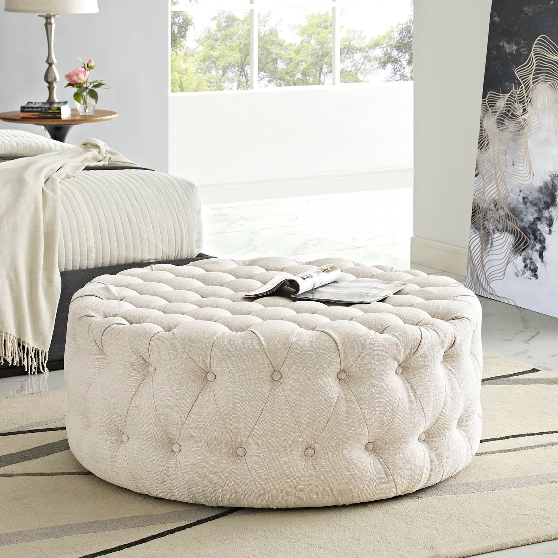 Round brown tufted fabric ottoman with button tufting; plush, versatile footrest or extra seating.