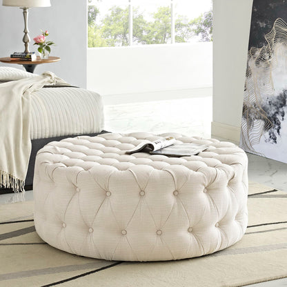 Round brown tufted fabric ottoman with button tufting; plush, versatile footrest or extra seating.