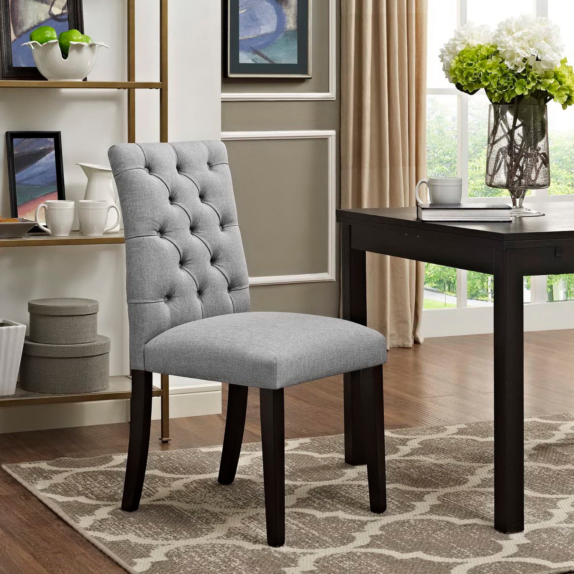 Light grey tufted dining chair with dark wood legs and tall back, beside a dark wood table in a modern dining room.