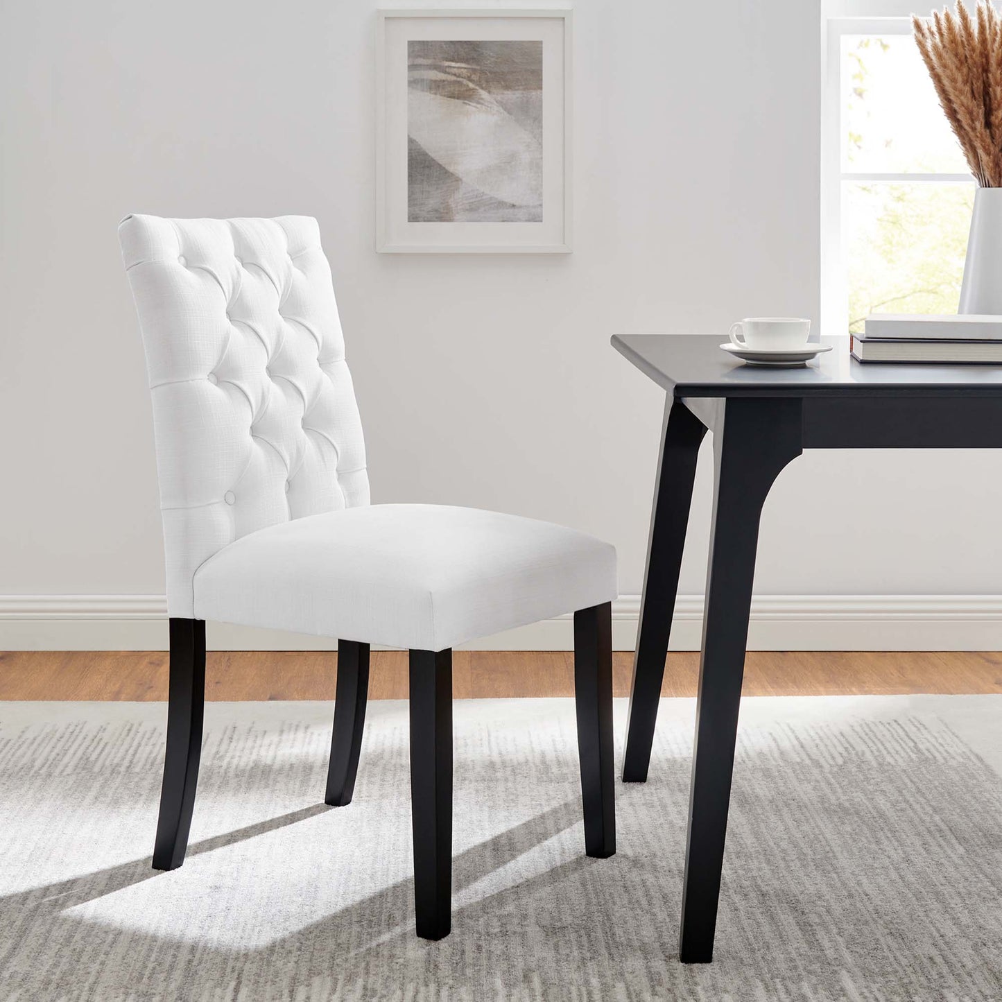 White tufted dining chair with dark wood legs beside a black modern table in a bright dining room.