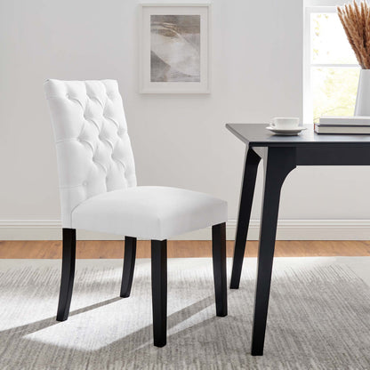 White tufted dining chair with dark wood legs beside a black modern table in a bright dining room.