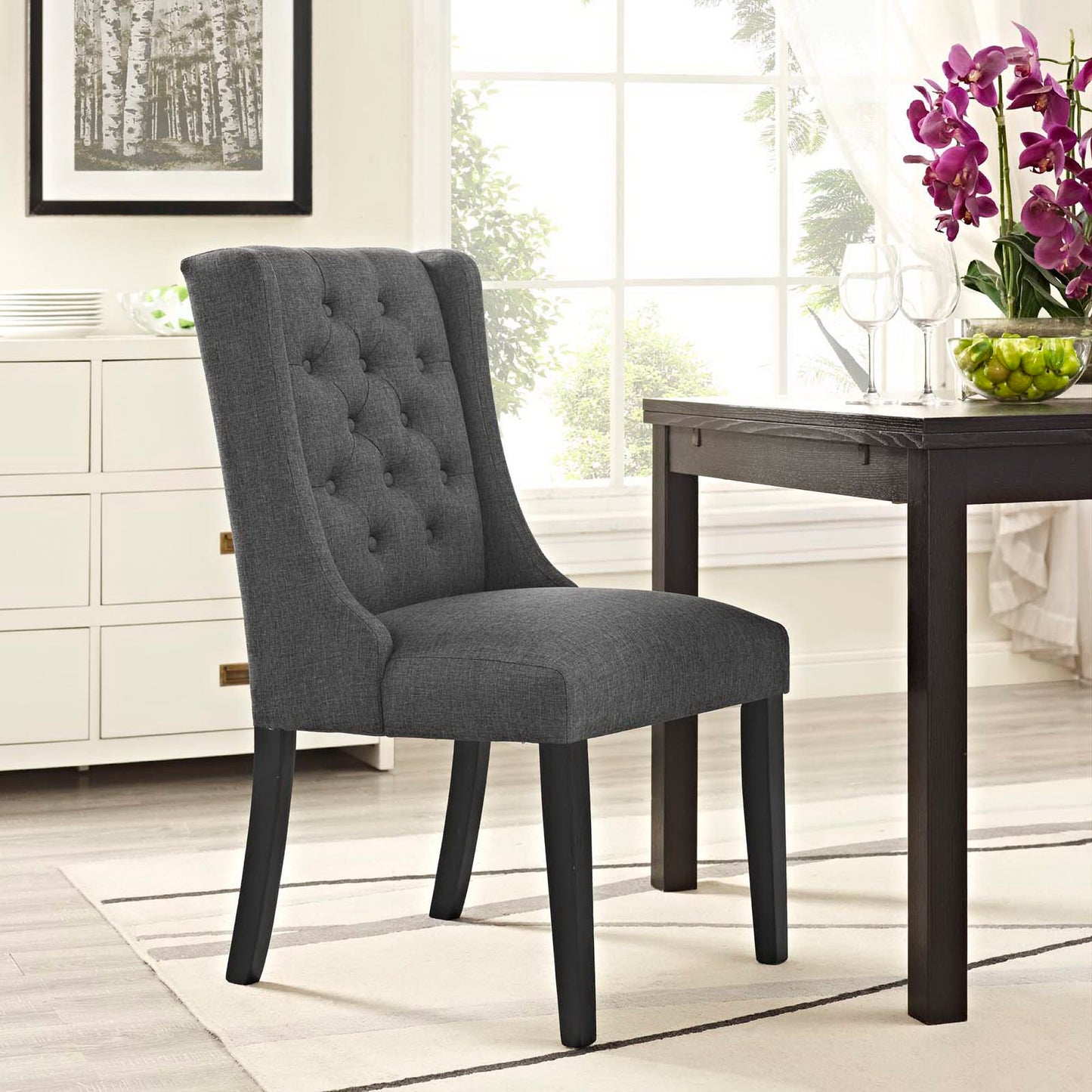 Gray button-tufted fabric dining chair with dark wood legs in a bright dining room.