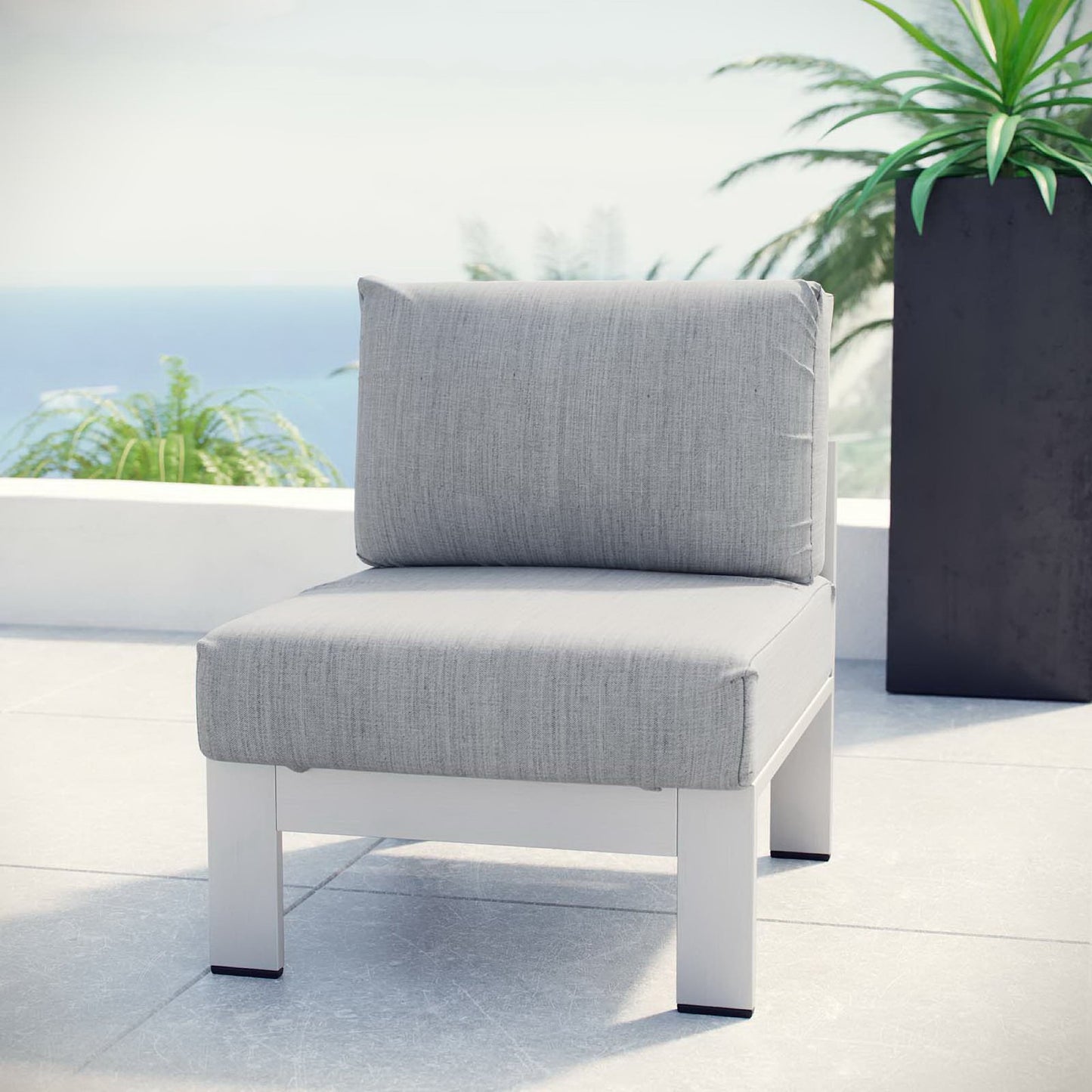 Armless outdoor aluminum chair with light gray cushions on a terrace with an ocean view