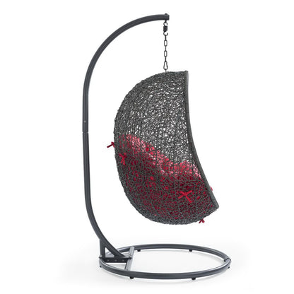 Gray woven hanging egg chair with red cushions on curved metal stand for outdoor lounging.