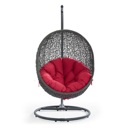 Red woven hanging egg chair with a plush red cushion on a circular metal stand.