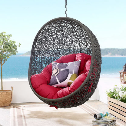Outdoor patio swing chair with a stand, dark gray frame and red cushions, floral pillow, on a seaside patio.