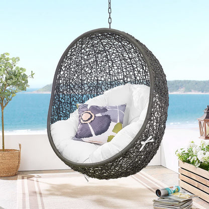 Dark gray woven outdoor swing chair with stand, white cushions and a purple accent pillow on a balcony