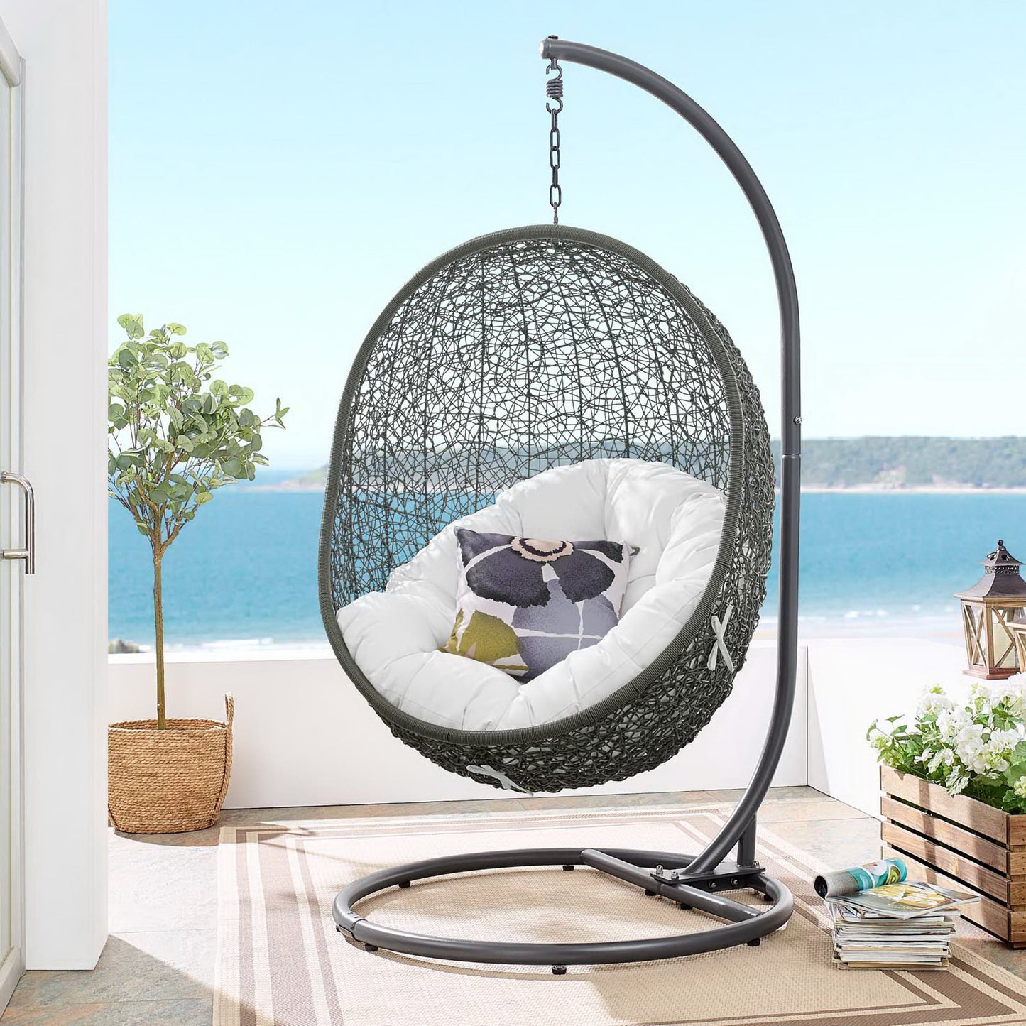 Grey woven outdoor swing chair with white cushions on a curved metal stand, on a patio.