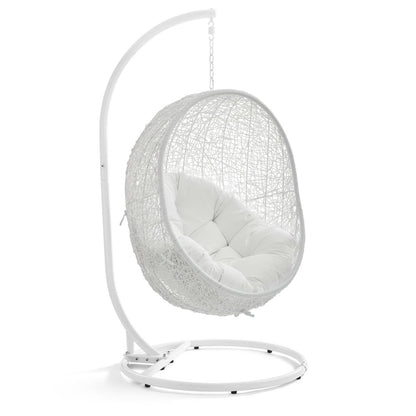 White hanging egg chair with woven rattan shell, plush white cushion & curved metal stand.