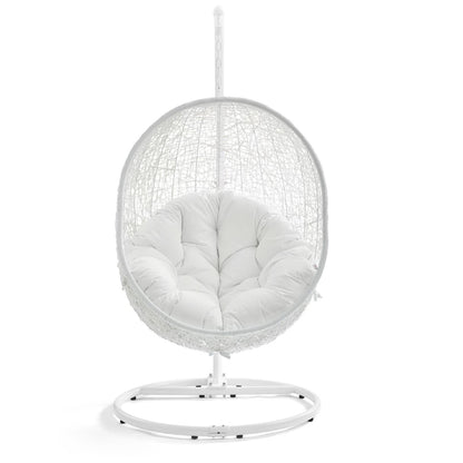 White hanging egg chair with woven rattan frame and plush white cushion on a circular metal stand.