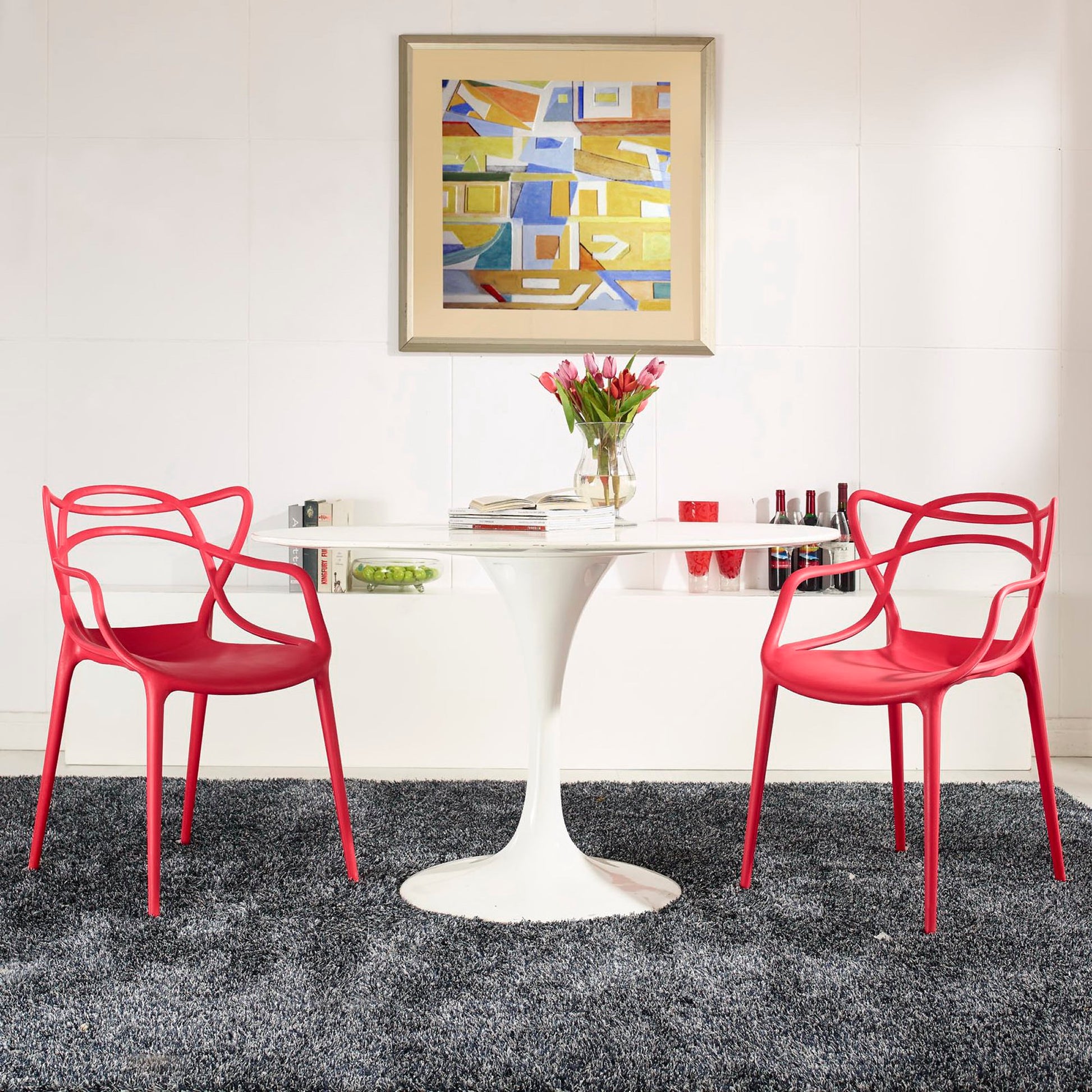 Red molded plastic chairs with a white tulip pedestal table, vase of pink tulips, and abstract art on a white wall.
