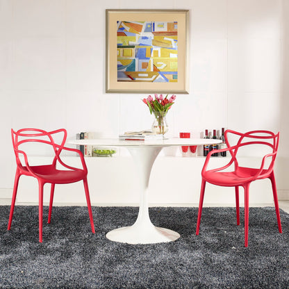 Red molded plastic chairs with a white tulip pedestal table, vase of pink tulips, and abstract art on a white wall.