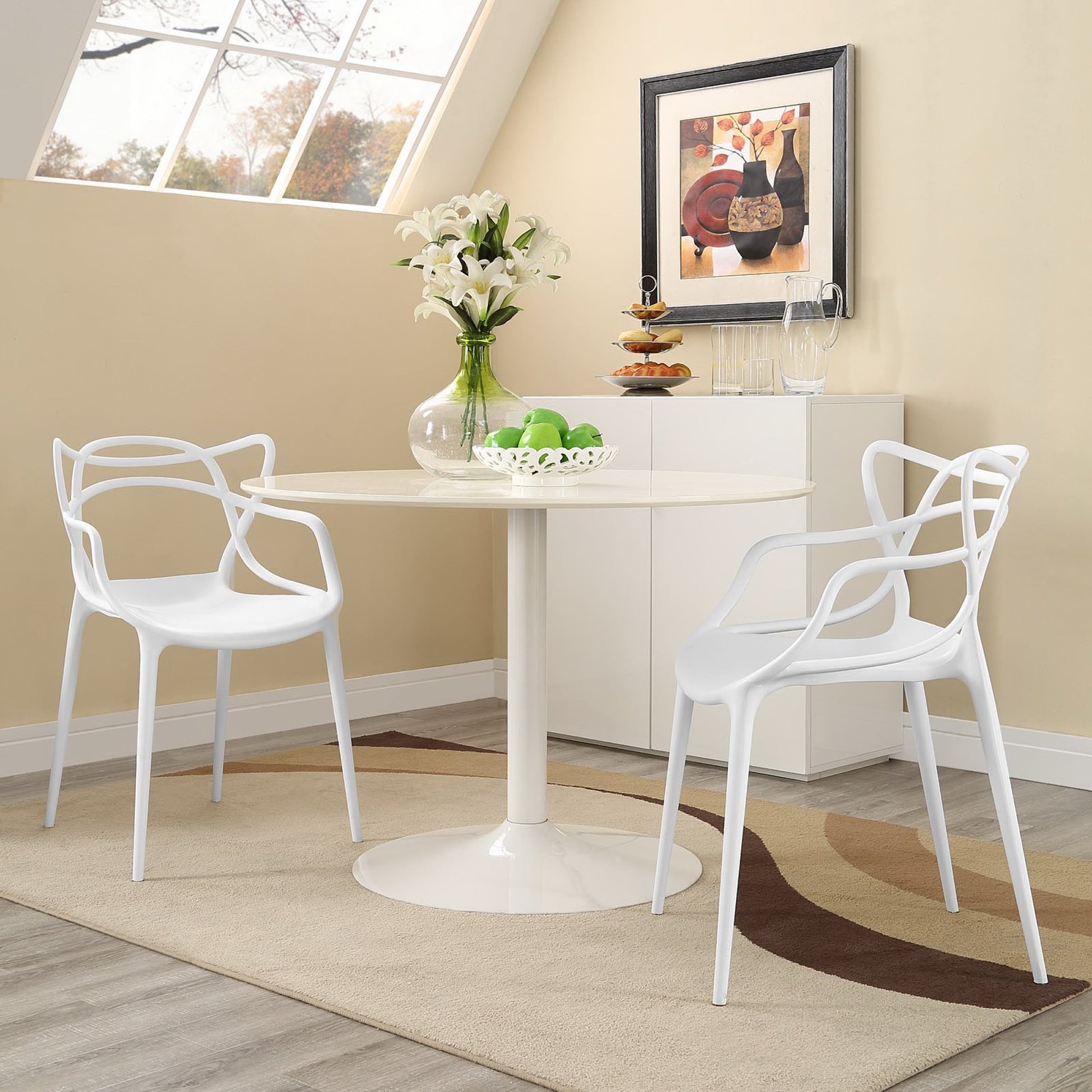 Two sculptural white dining chairs with a vase of white lilies and a fruit bowl in a sunlit beige dining nook.