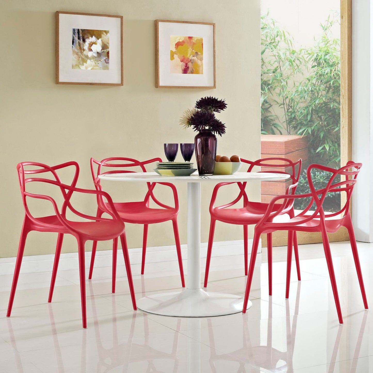 Red modern dining chairs surround a white round pedestal table with a tall dark vase centerpiece; beige walls and framed art.