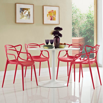 Red modern dining chairs surround a white round pedestal table with a tall dark vase centerpiece; beige walls and framed art.