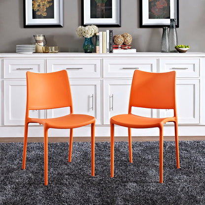 Two bright orange molded plastic dining chairs with slender metal legs on a gray rug in a modern kitchen with white cabinetry.