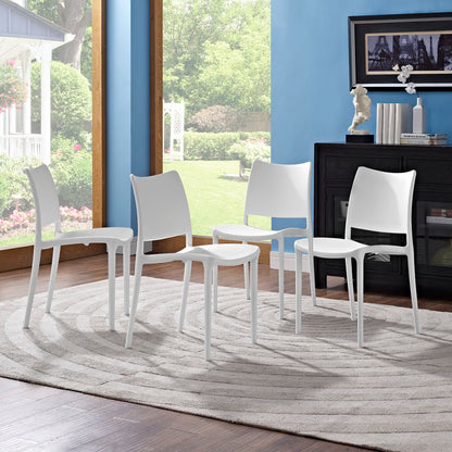 Four white modern plastic dining chairs around a circular rug in a sunlit room with blue walls and a black sideboard.