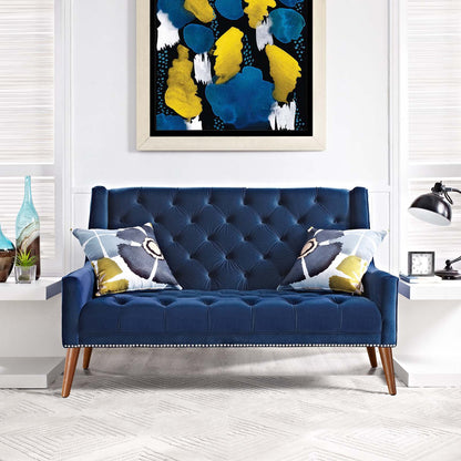 Navy tufted loveseat with nailhead trim and wooden legs, two geometric pillows; abstract blue-yellow art on white wall.