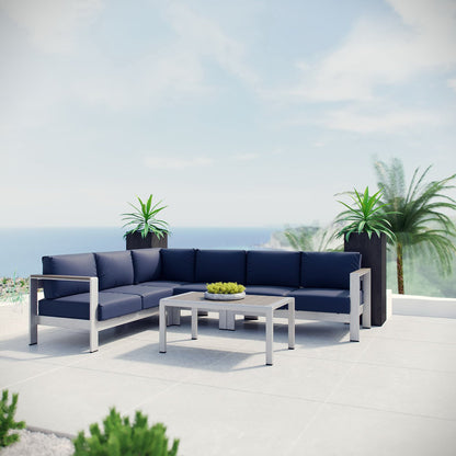 Navy outdoor sectional with silver metal frame and rectangular coffee table on a sunlit terrace with plants and ocean view.
