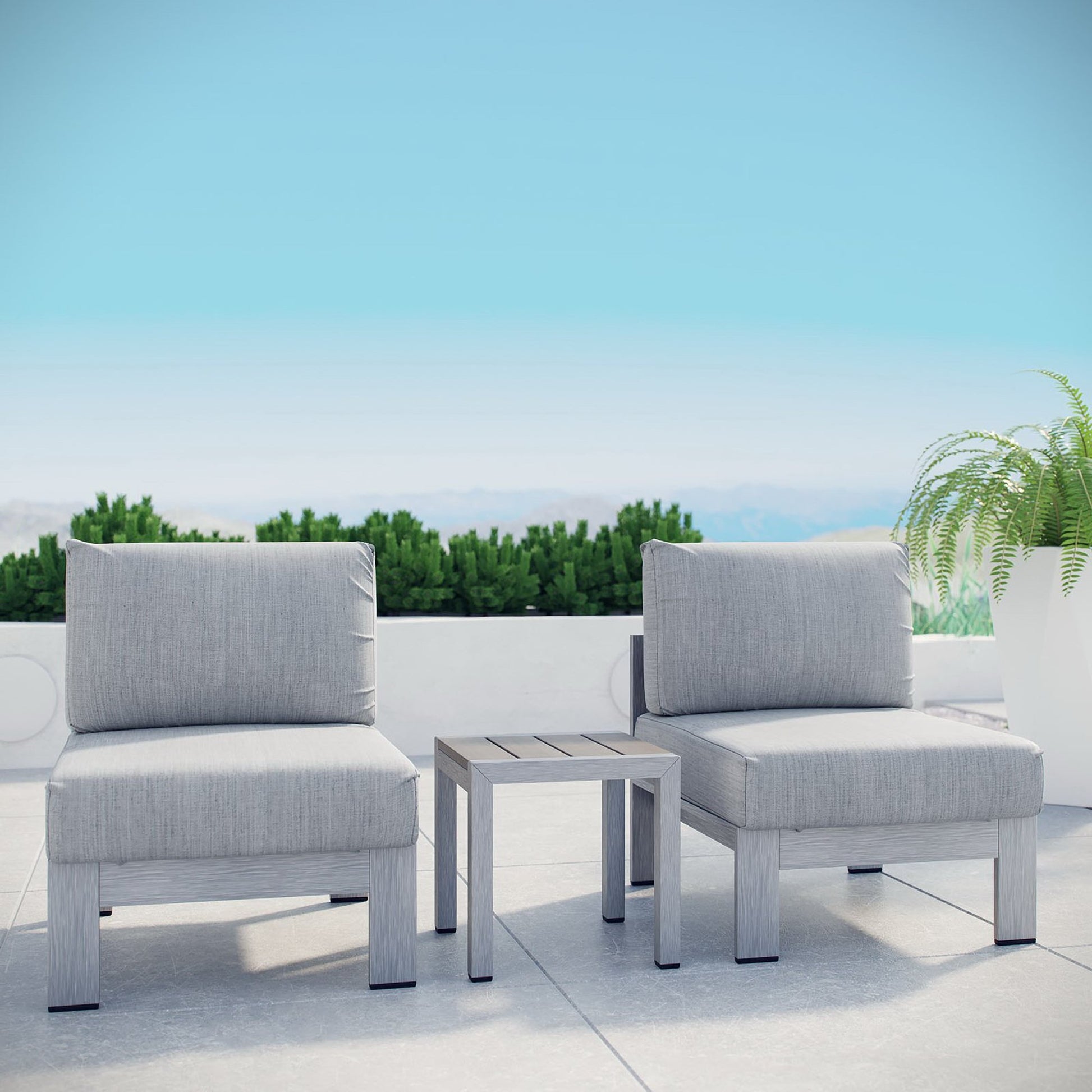 Three-piece gray outdoor aluminum sectional sofa set with cushions and a small side table on a white patio, with a fern in a pot to the right.