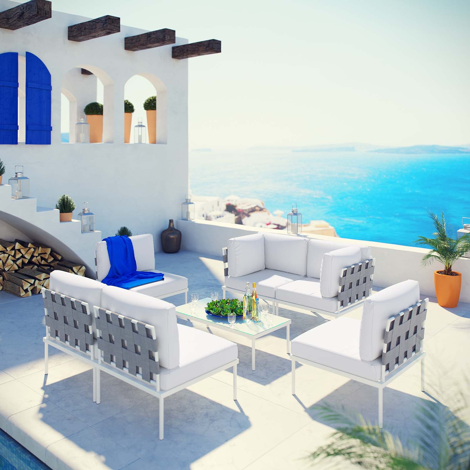 White 7-piece outdoor patio aluminum sectional sofa set with gray woven backs and cushions, glass coffee table, on a sunlit terrace with blue sea view.