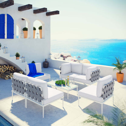 White 7-piece outdoor patio aluminum sectional sofa set with gray woven backs and cushions, glass coffee table, on a sunlit terrace with blue sea view.