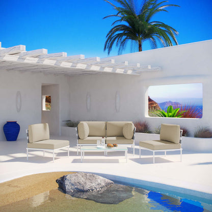 White outdoor seating set with beige cushions & bolster pillows on a sunlit stucco patio by a pool, palm tree & blue sky.