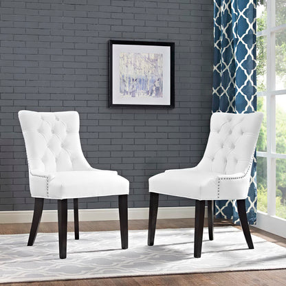 Pair of white tufted dining chairs with dark wood legs and nailhead trim in a gray brick room with blue patterned curtains.