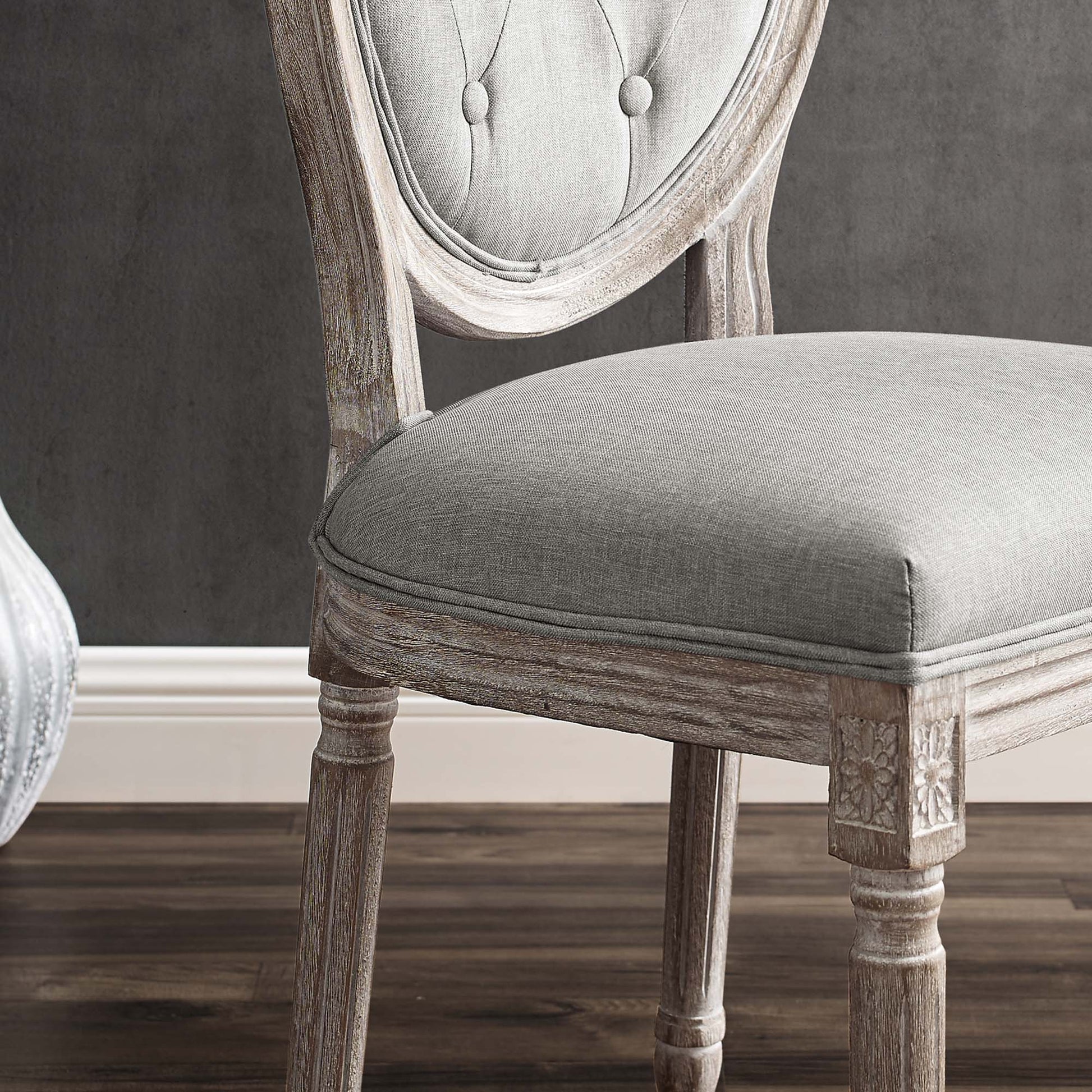 Antique gray upholstered dining side chair with tufted back, carved wood legs and weathered finish on dark wood floor.