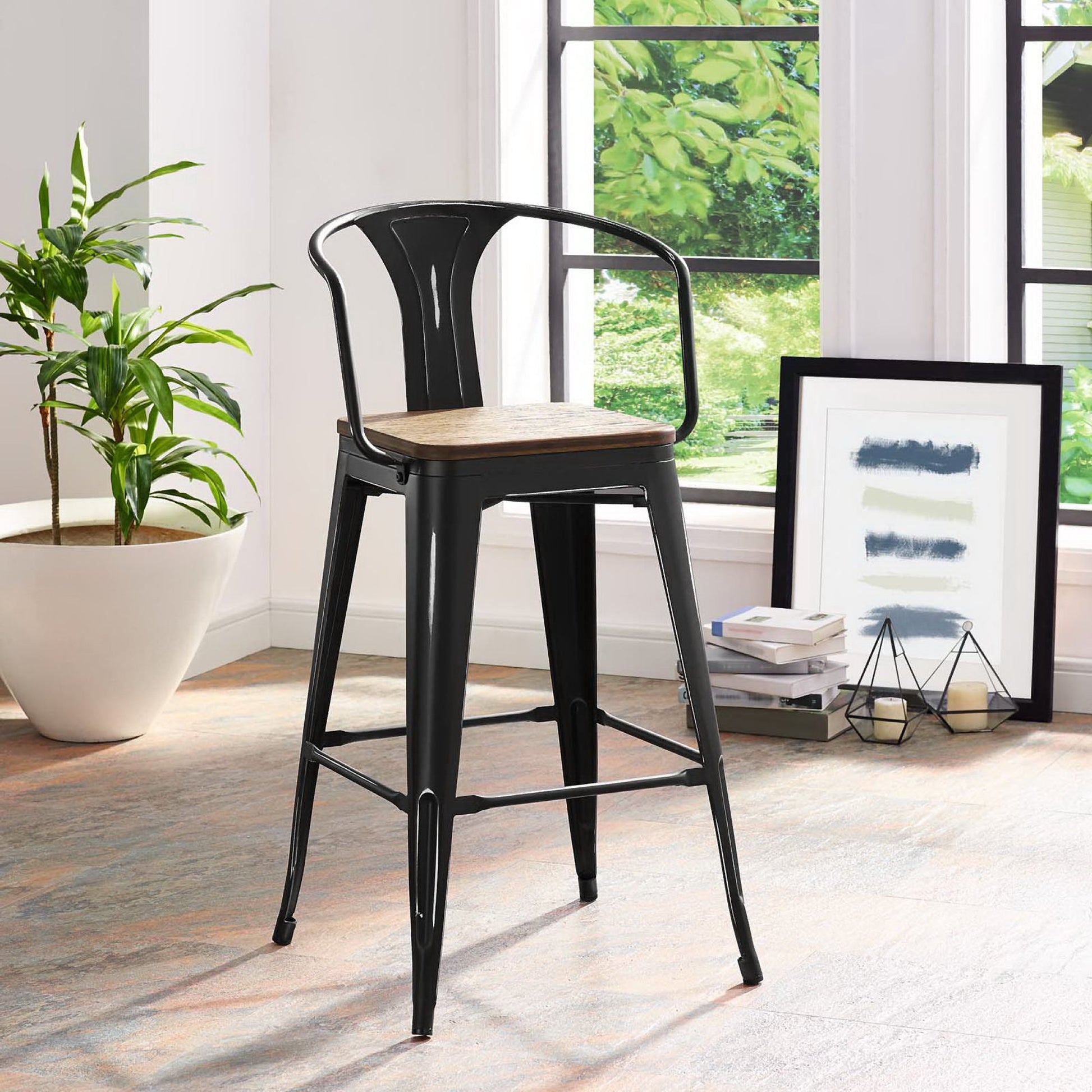Black metal bar stool with natural wood seat, Tolix-style design, curved backrest and footrest in a bright room.